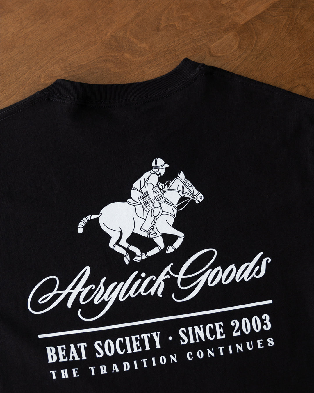 Illustration of a polo player riding a horse while holding an MPC beat machine, blending tradition, music culture with the words Acrylick Goods, Beat Society since 2003, the tradition continues.